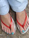 Girl in jeans and flip flops demonstrates her toes and blue toenails outdoors