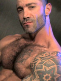 Hairy man Junior Stellano with tattooed arms takes off his jeans and jerks his d