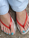 Girl in jeans and flip flops demonstrates her toes and blue toenails outdoors