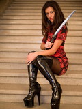Eye-popping brunette in red dress and thigh high black boots made of latex poses
